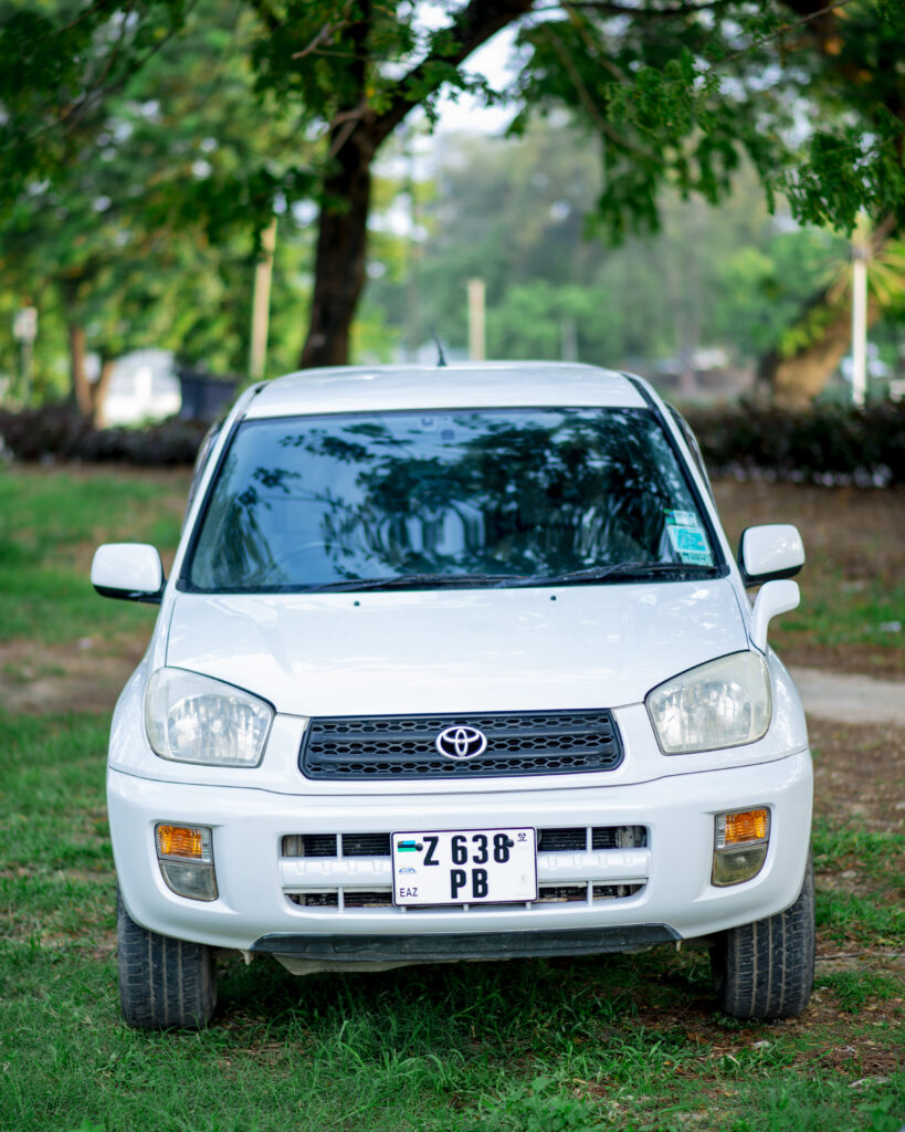 White Toyota RAV4 parked on grass under trees, front view
